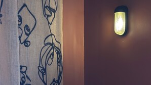 Une salle de bain avec une baignoire blanche, un mur orné de dessins abstraits, une étagère avec des bougies et une bouteille, et un luminaire fixé au mur.