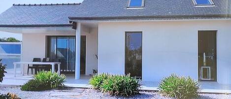 Ein modernes Haus mit Satteldach, großen Fenstern und einem gepflegten Garten mit Kies und Pflanzen.