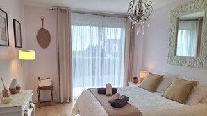 Une chambre à coucher avec un grand lit, un lustre, un miroir et une fenêtre ornée de rideaux légers.