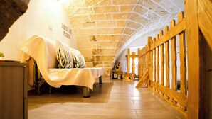 A room with a high arched ceiling, wooden flooring, a bed with a white bedspread, a small table with a vase, and a wooden railing along one wall. - Once upon a time. Apartment with typical star vault and barrel vault. (Nardò)