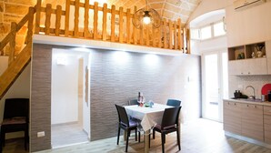 A dining area with a table and chairs, a wooden staircase, and a kitchen area with cabinets and a countertop. - Once upon a time. Apartment with typical star vault and barrel vault. (Nardò)