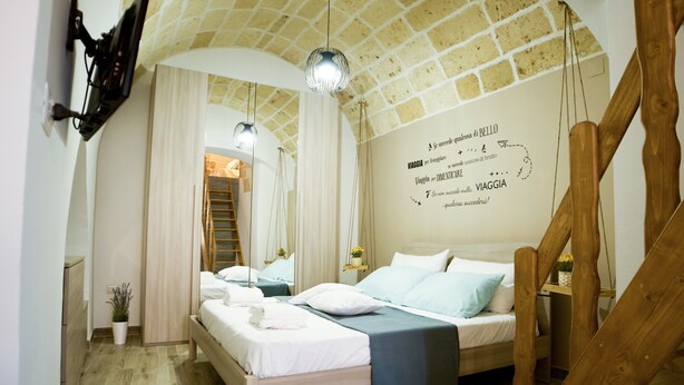 A bedroom with a wooden bed, a mirror, a wall with text, and a staircase. - Once upon a time. Apartment with typical star vault and barrel vault. (Nardò)