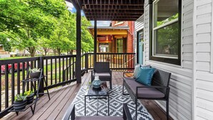 A covered deck with outdoor furniture and a patterned rug.