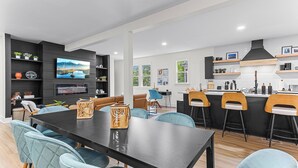 A modern kitchen with a central island, bar stools, and a dining area with a large table and chairs.