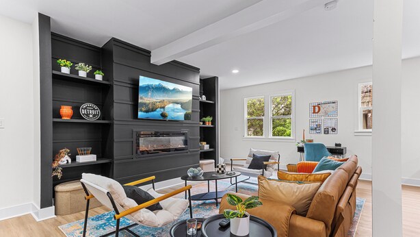 A modern living room with a large flat-screen TV, black shelving, a brown leather sofa, and a coffee table.