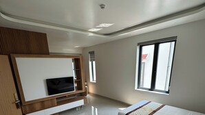 Habitación de hotel con dos camas, televisor, aparador de madera y ventana.