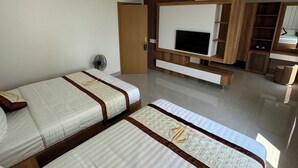 Habitación de hotel con dos camas, televisión, armario y una pequeña zona de estar.
