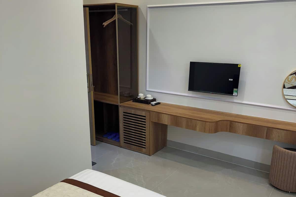 Um quarto moderno com cama, escrivaninha, televisão e guarda-roupa.
