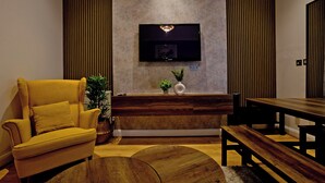 A modern living room with a sofa, a wooden dining table, and a flat-screen TV mounted on the wall. - Imperial Argyle Square Apartment (London)