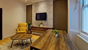 A modern living room with a wooden coffee table, a yellow sofa, and a flat-screen TV mounted on the wall. - Imperial Argyle Square Apartment (London)