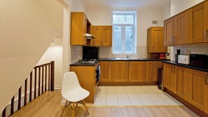 A modern kitchen with wooden cabinets, a white chair, and a window. - Imperial Argyle Square Apartment (London)
