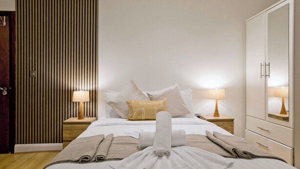 A hotel room with a neatly made bed, two bedside tables with lamps, a wardrobe, and a striped wall. - Imperial Argyle Square Apartment (London)