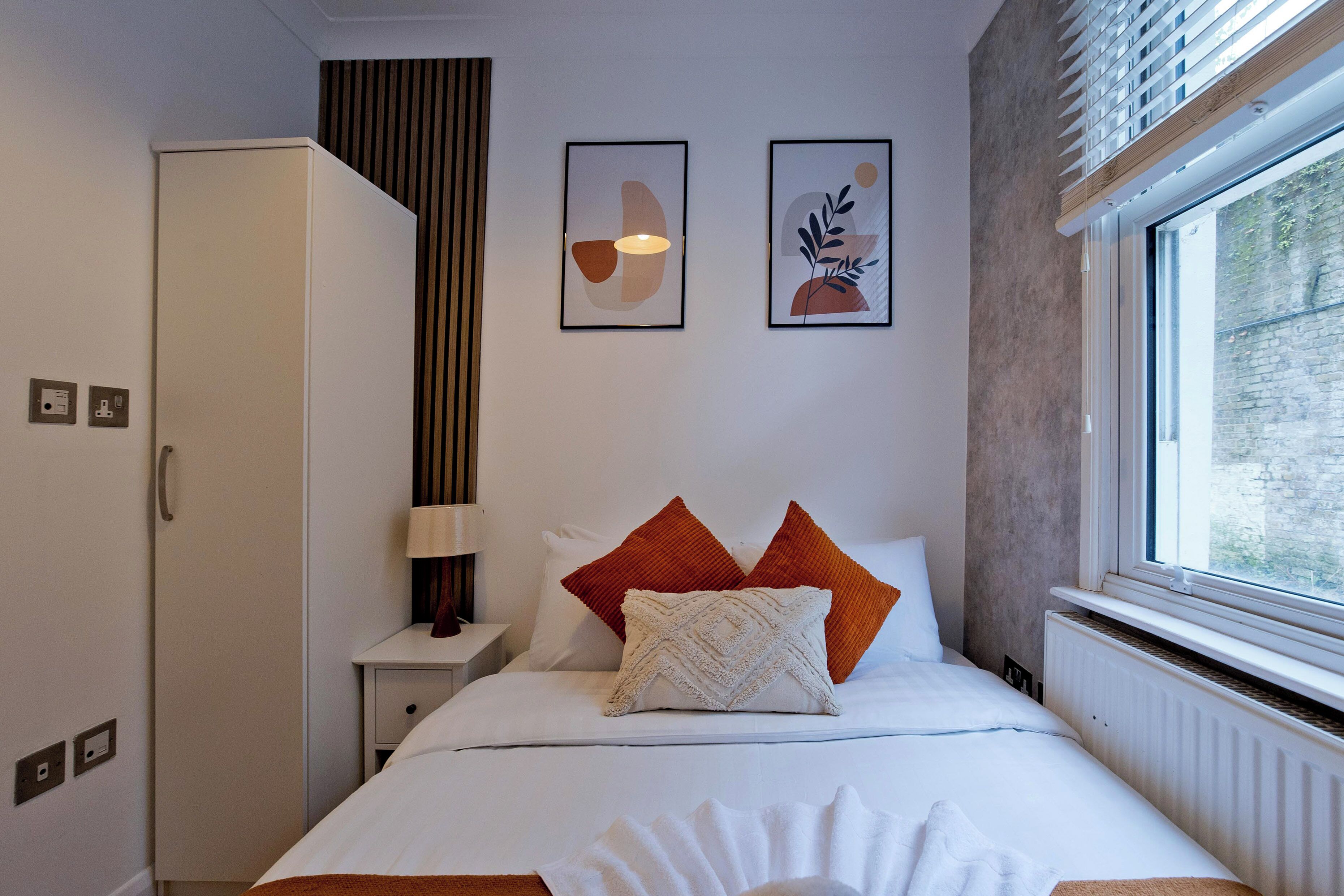 A bedroom with a bed, a nightstand, a wardrobe, and two framed artworks on the wall.