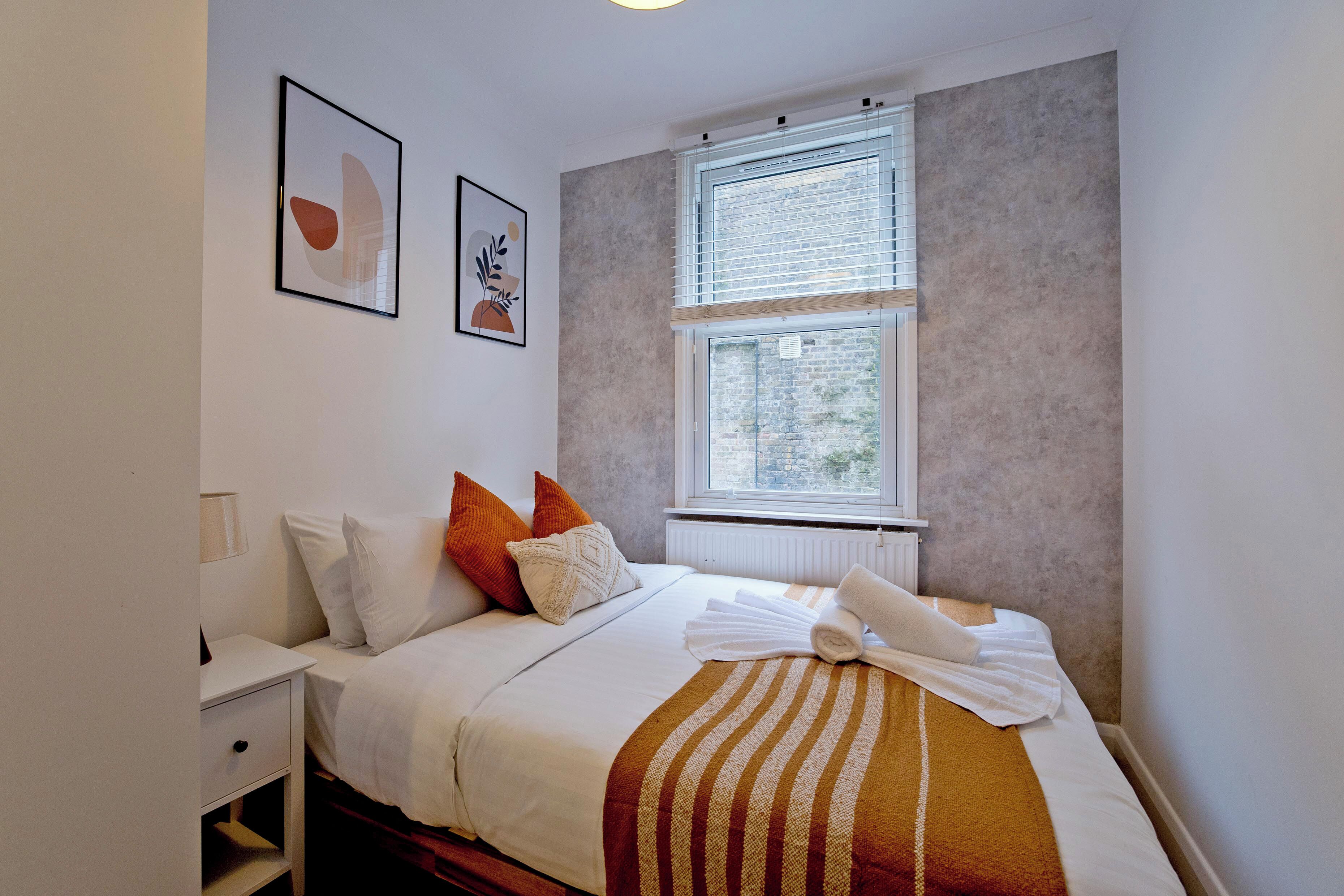 A neatly arranged hotel room with a bed, pillows, a bedside table, and a window with blinds.