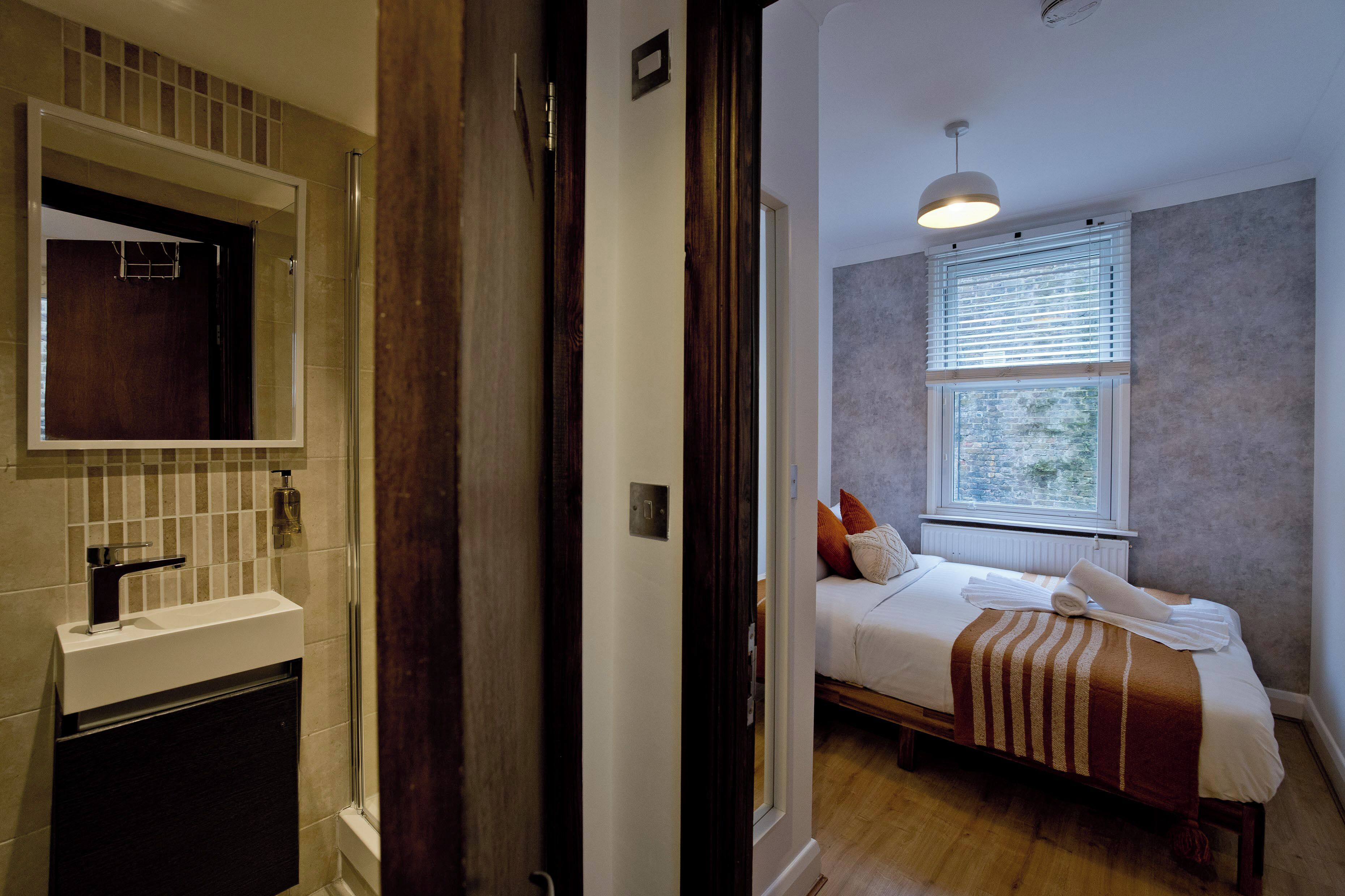 A hotel room with a bathroom, a bed with a striped blanket, and a window with blinds.