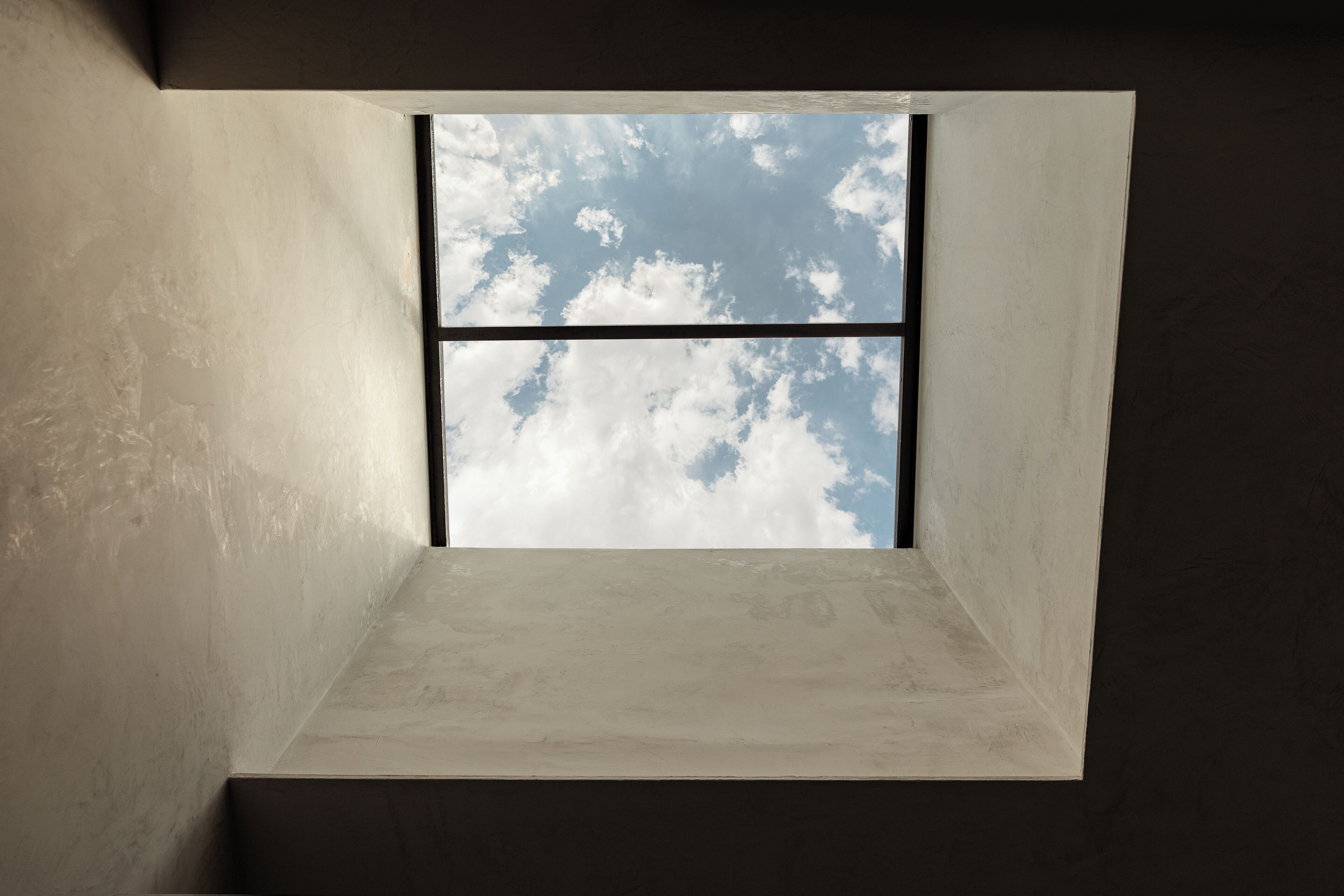 Ein Zimmer mit einem Fenster, das von einer weißen Wand umrahmt wird und einen Blick auf den Himmel und die Wolken bietet.