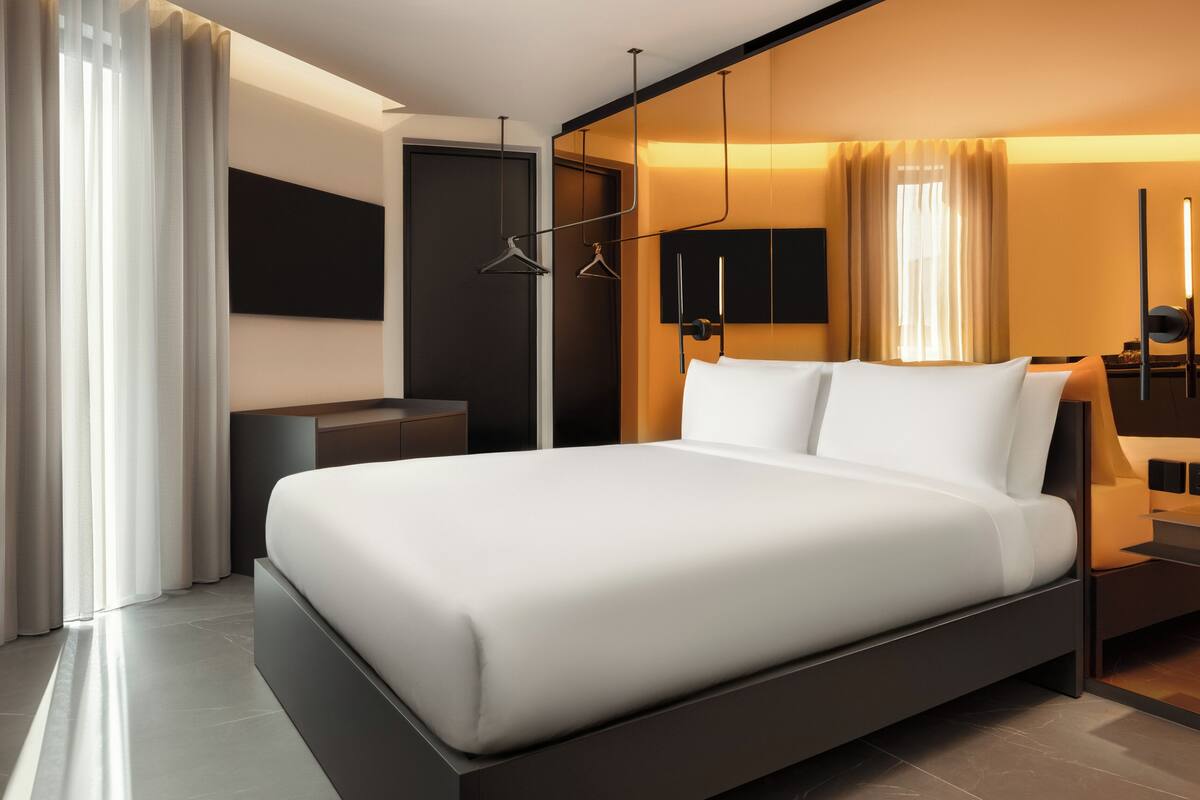 Una habitación de hotel moderna con una cama grande, una mesita de noche, un televisor de pantalla plana y un armario.