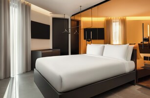 Una camera d'albergo moderna con un letto grande, un comodino, una televisione a schermo piatto e un armadio.