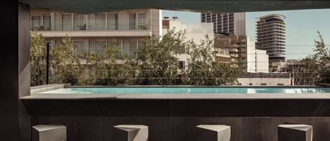 A modern building with a rooftop pool, surrounded by greenery and urban high-rises.