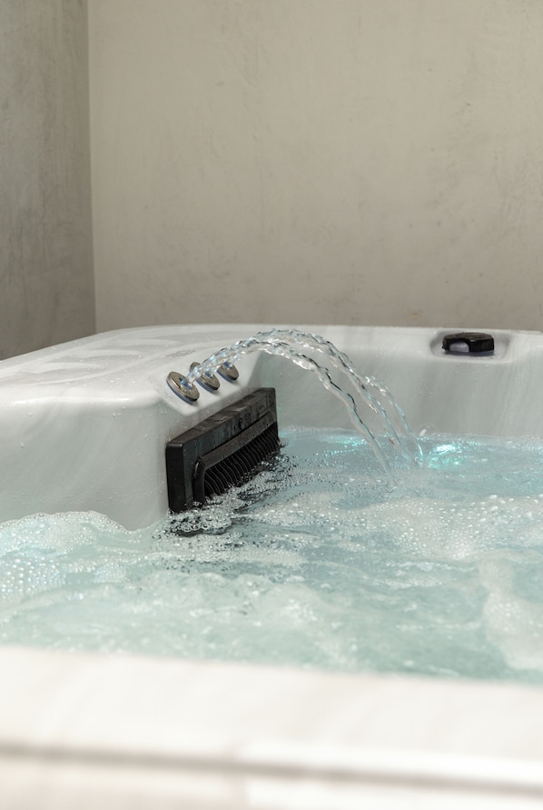 Una bañera de hidromasaje con agua fluyendo, un panel de control y una pared al fondo.