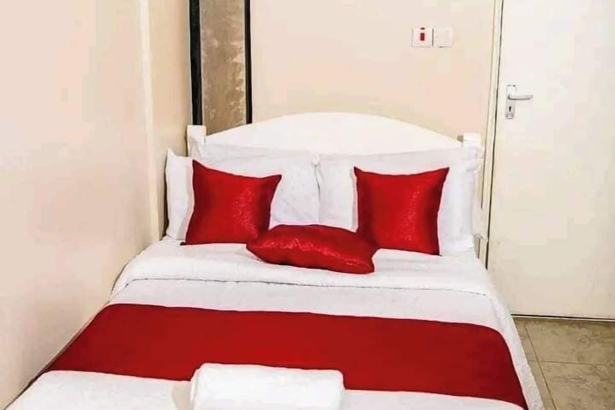 Una cama bien hecha con ropa de cama blanca y roja, cabecera blanca y una puerta blanca al fondo.