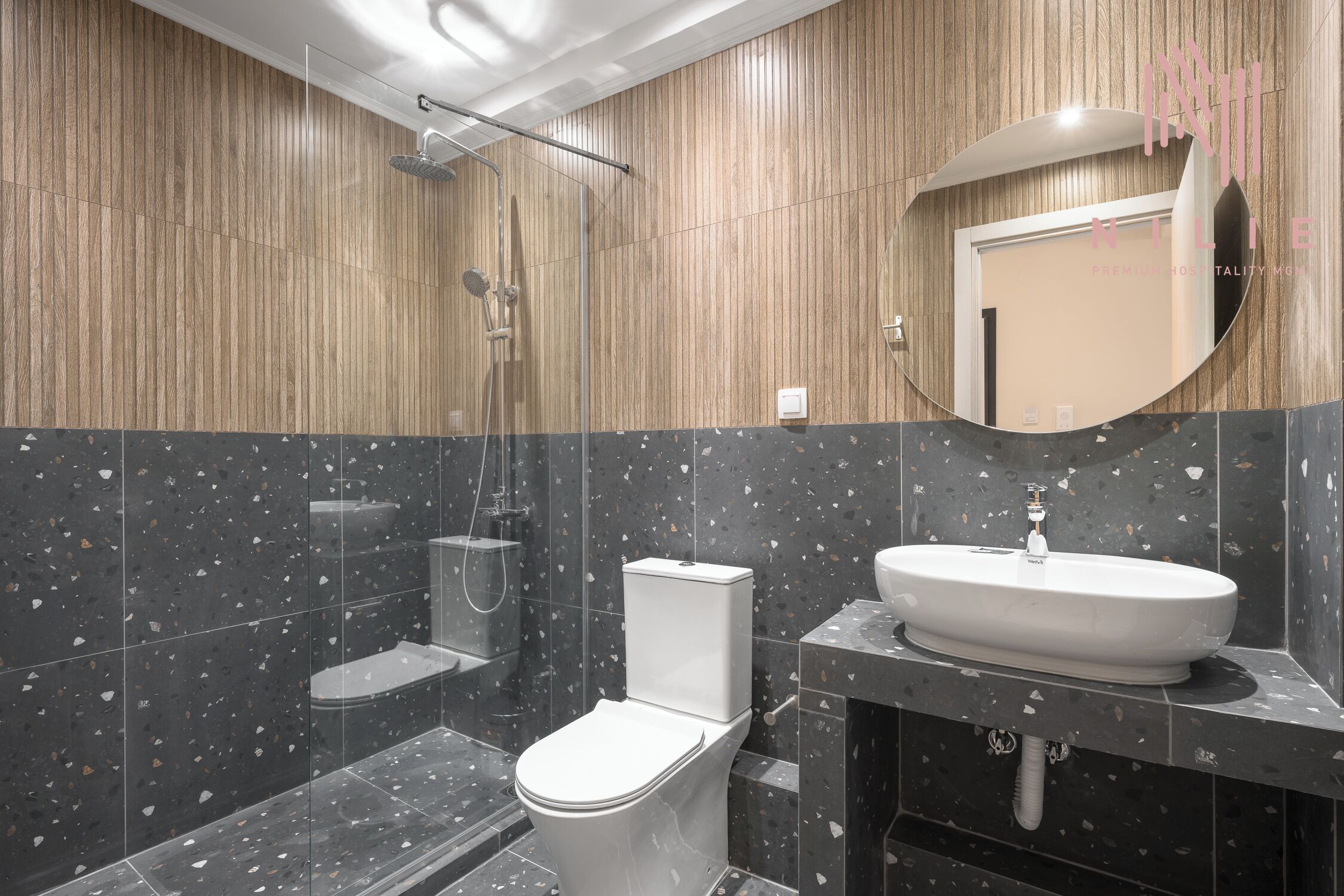 Un baño moderno con pared de paneles de madera, un inodoro independiente, una ducha con cerramiento de vidrio y un lavabo con espejo.