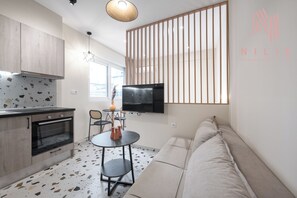 A modern kitchen with a built-in oven, a dining area with a round table and chairs, and a large window with vertical blinds.