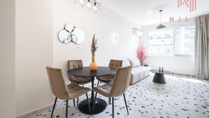 A modern dining area with a round table, six chairs, and a vase of flowers. There is a sofa and a small table with candles in the background. - Phedra Studios Nilie Hospitality MGMT (Thessaloniki)