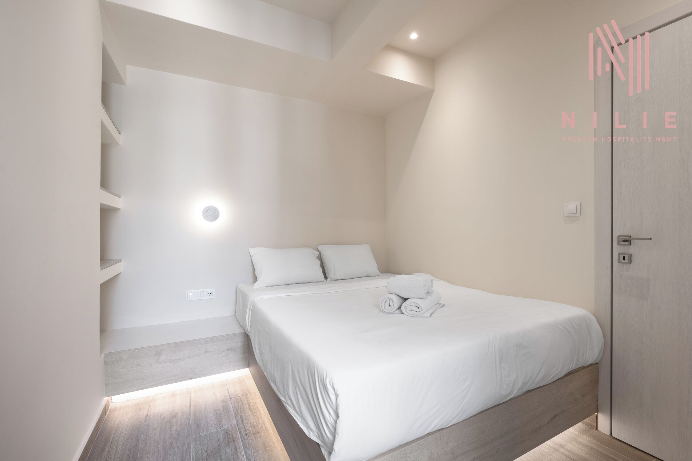 A modern bedroom with a bed, a bedside table, a nightstand, and a built-in shelf unit.