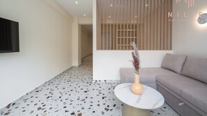 A modern interior with a sofa, a round table with a vase, a TV mounted on the wall, and a terrazzo floor. - Phedra Studios Nilie Hospitality MGMT (Thessaloniki)