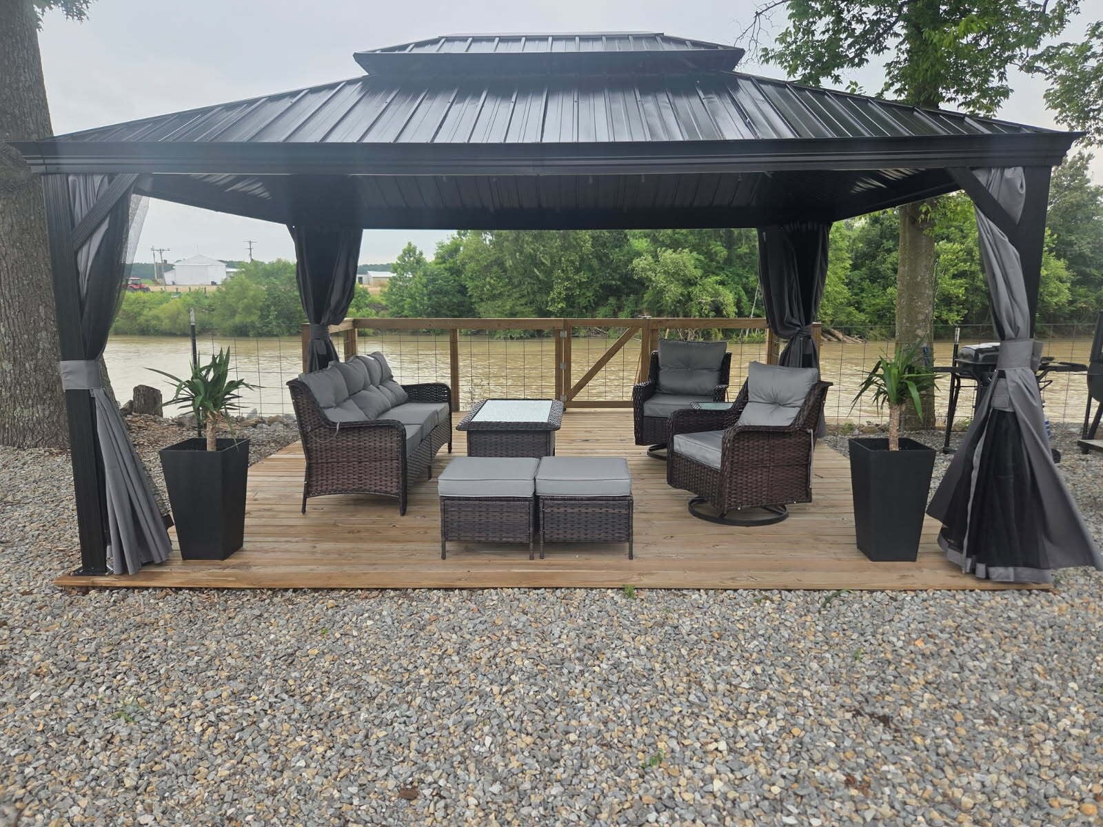 A covered outdoor seating area with wicker furniture and a view of a river.