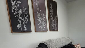 En mörkgrå soffa med en grå pläd och en svart kudde. Ovanför soffan hänger tre inramade konstverk med blommotiv på väggen.