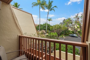 A balcony with a view of a parking lot, palm trees, and a clear sky.