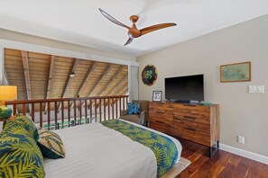 Ein Schlafzimmer mit Bett, Holzbalkendecke, Deckenventilator, Fernseher und Kommode.
