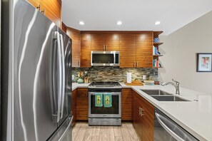 A modern kitchen with stainless steel appliances, wooden cabinets, and a tiled backsplash.