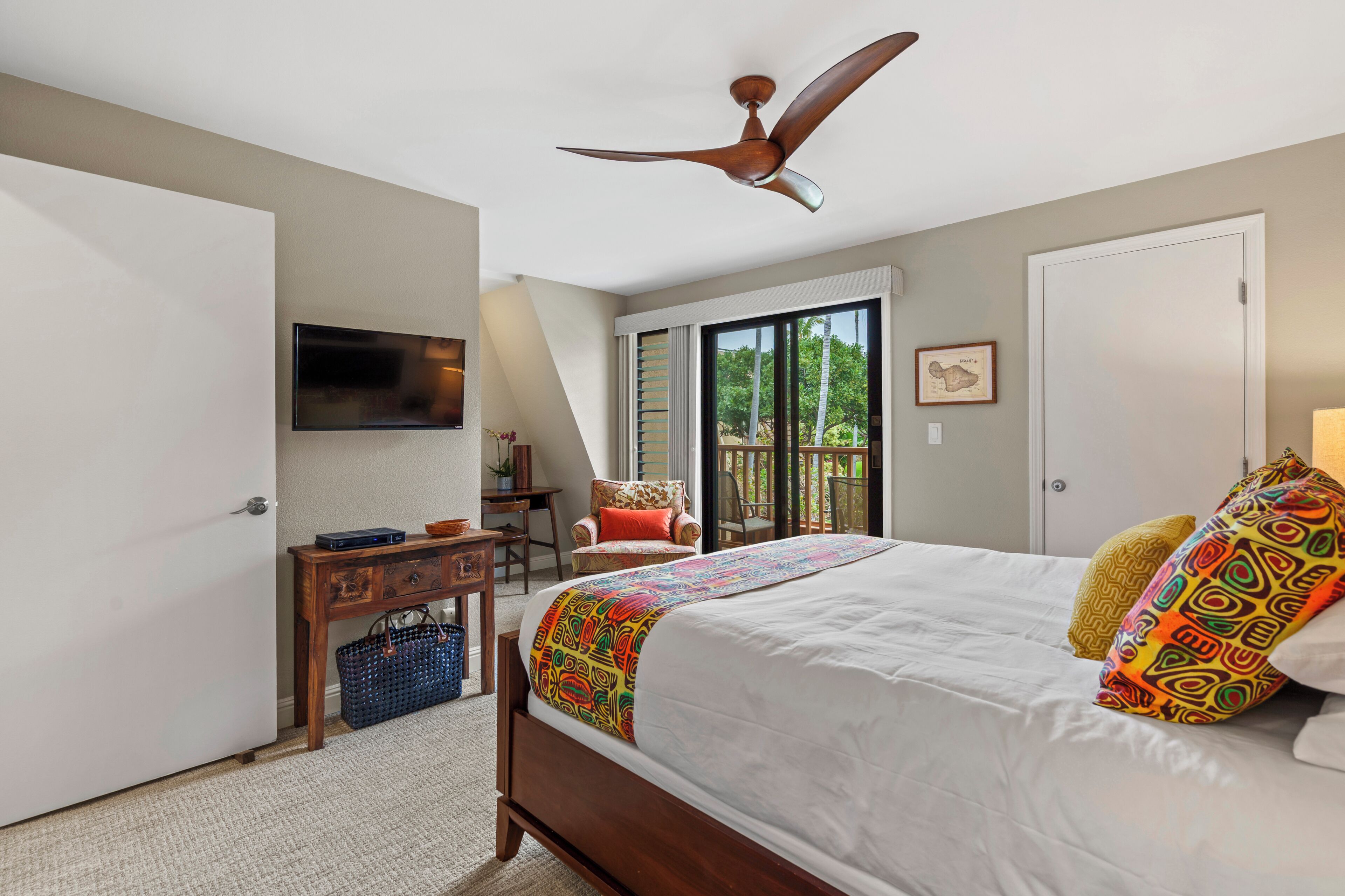 A bedroom with a bed, a ceiling fan, a desk, a chair, and a sliding glass door to the outside.