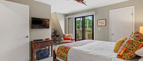 A bedroom with a bed, a ceiling fan, a desk, a chair, and a sliding glass door to the outside.