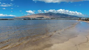 Una playa con aguas cristalinas y poco profundas, una orilla arenosa y una montaña al fondo.
