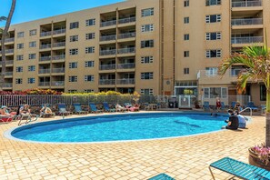 Ein Swimmingpool mit Liegestühlen und ein mehrstöckiges Gebäude im Hintergrund.