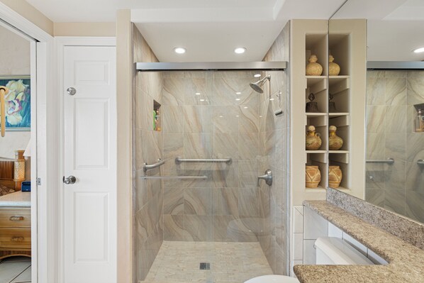 A bathroom with a shower, vanity, and storage shelves. - Menehune Shores #609 - Top-Floor Oceanview Condo Steps from Beach (Kihei, Maui)