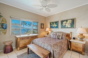 Ein Schlafzimmer mit einem Bett, Nachttischen, einer Bank, einem Deckenventilator, einem Fenster mit Blick und Kunstwerken an den Wänden.