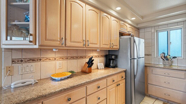 Cocina con armarios de madera, refrigerador de acero inoxidable, cafetera y un tazón de fruta sobre la encimera.