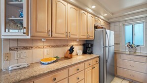 Cocina con armarios de madera, refrigerador de acero inoxidable, cafetera y un tazón de fruta sobre la encimera.