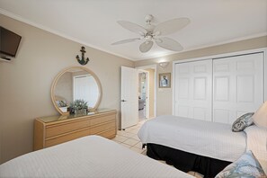 Un dormitorio con dos camas, un aparador, un ventilador de techo y una puerta que da a otra habitación.