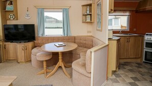 Un espacio habitable compacto con sofá, una mesita redonda, televisión, área de cocina con armarios y estufa, y ventana con cortinas.