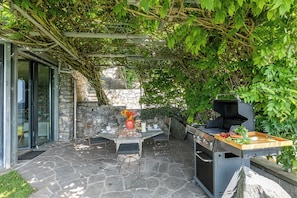 An outdoor patio with stone flooring, a table with chairs, a grill, and a pergola covered with climbing plants. - Villa Skyline - Pool - Lakeview - Privacy (Lugano)