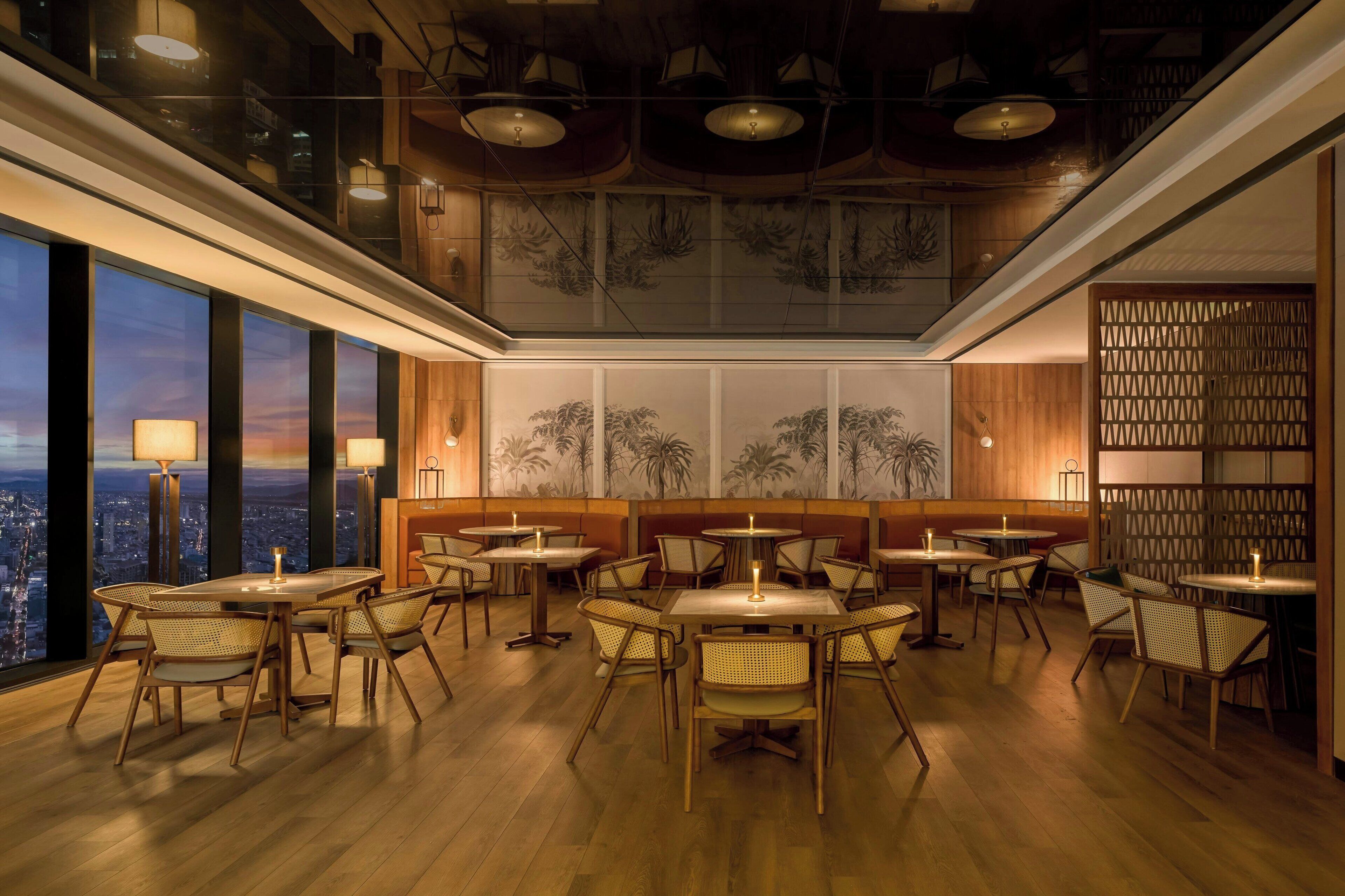 A restaurant with high tables and chairs, a city view, and a ceiling with a geometric pattern.