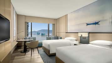 A hotel room with two beds, a TV, a small table, and a view of a cityscape.