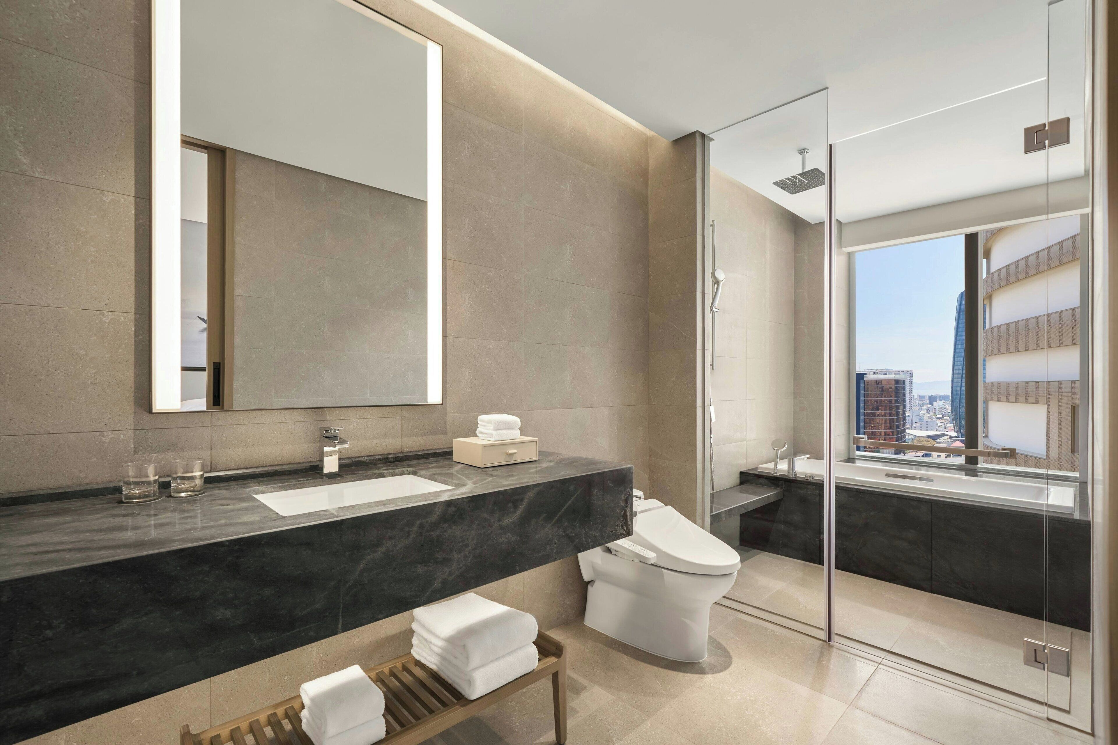 A modern bathroom with a large mirror, a sink, a toilet, and a glass-enclosed shower.