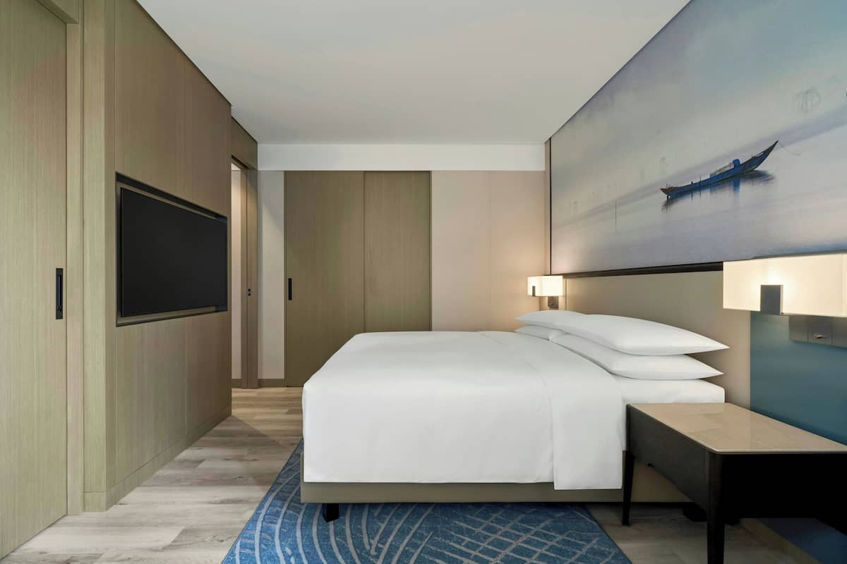 Een hotelkamer met een bed, een bureau, een aan de muur bevestigde televisie en een schilderij van een boot.
